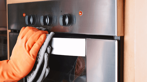 Person wearing an orange oven mitt opening a stainless steel oven.