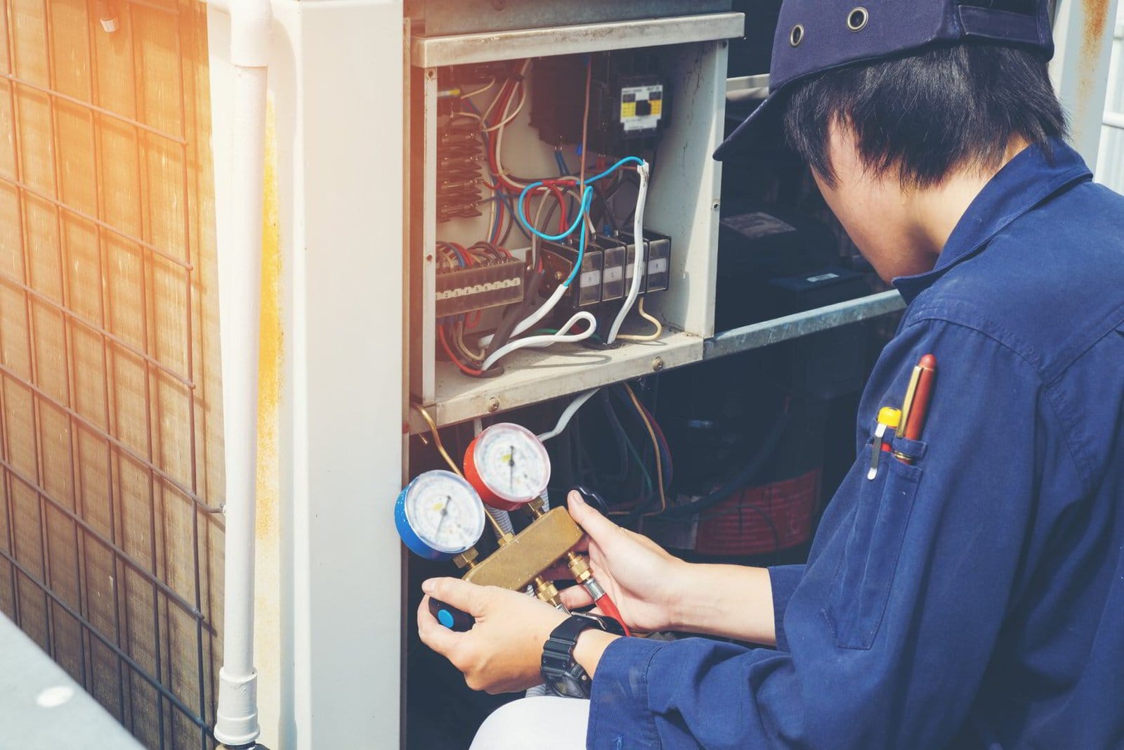 Technician servicing an air conditioning unit with pressure gauges and tools.