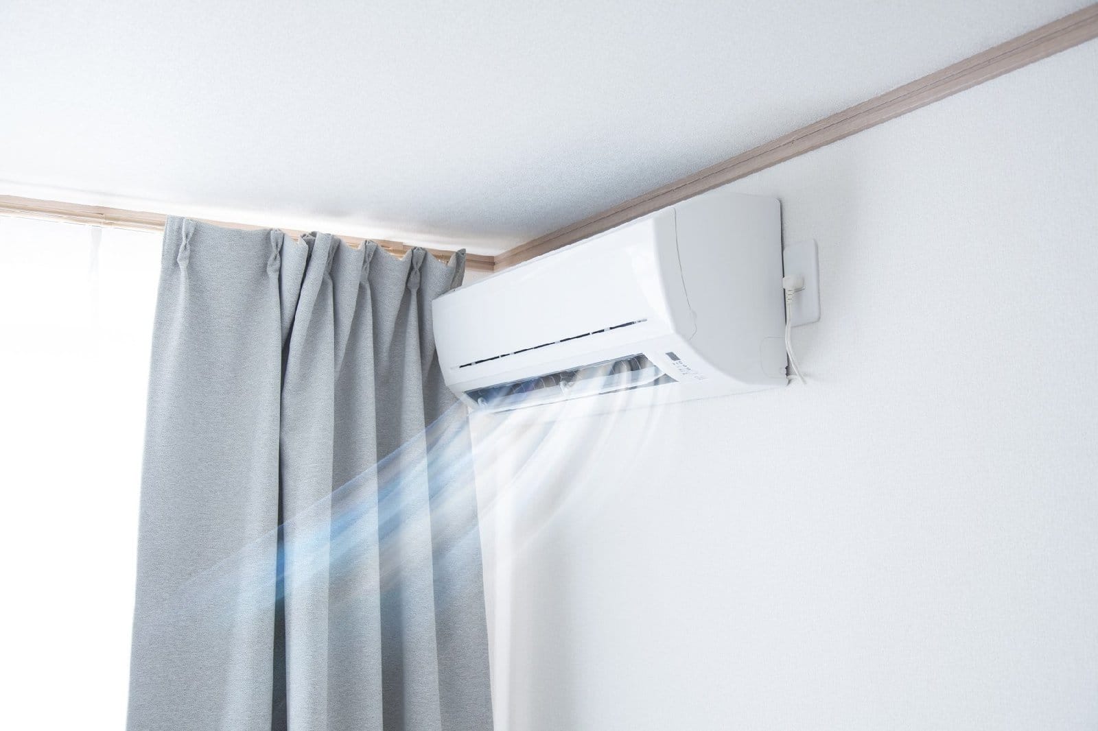 Air conditioner on wall with visible cool air flow and curtains.