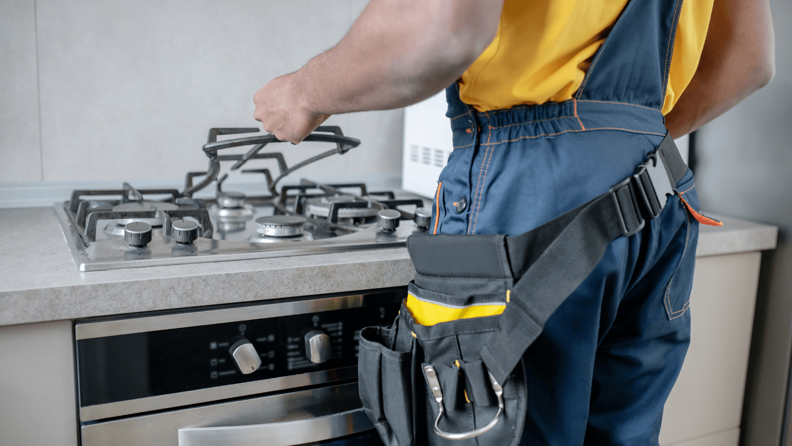 Repairman with tool belt working on a gas stove.