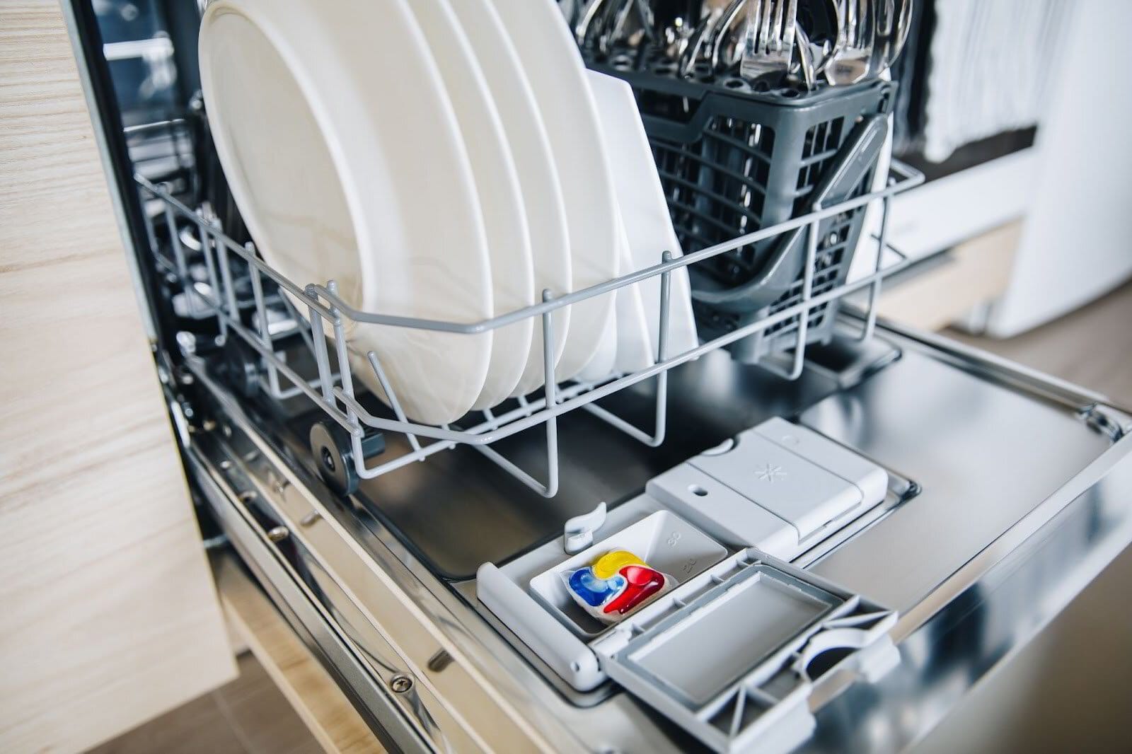An open dishwasher with clean dishes and a detergent pod.
