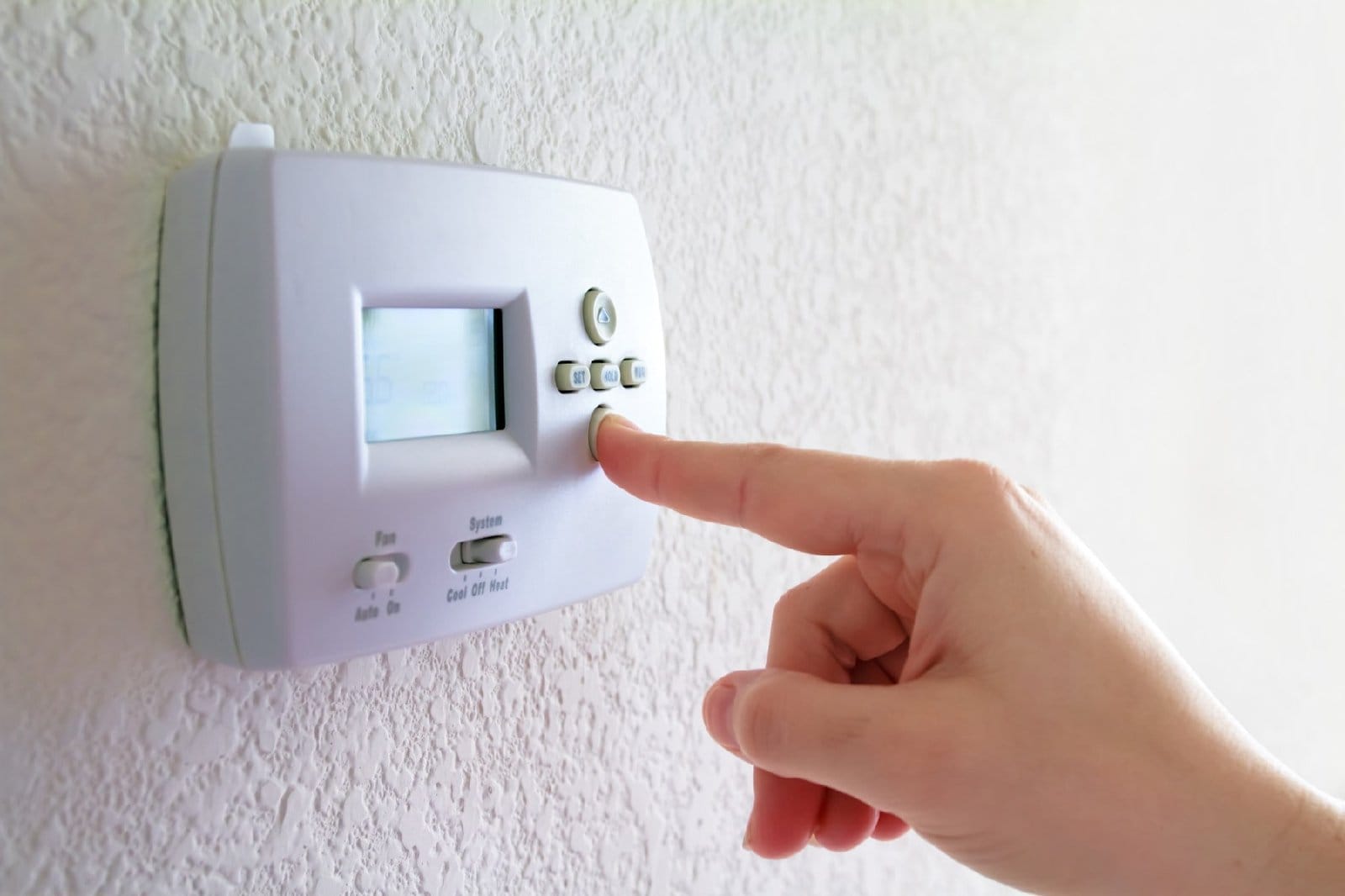 A person adjusting a wall-mounted thermostat.