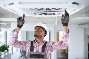 A black man working on an air conditioner in an office.