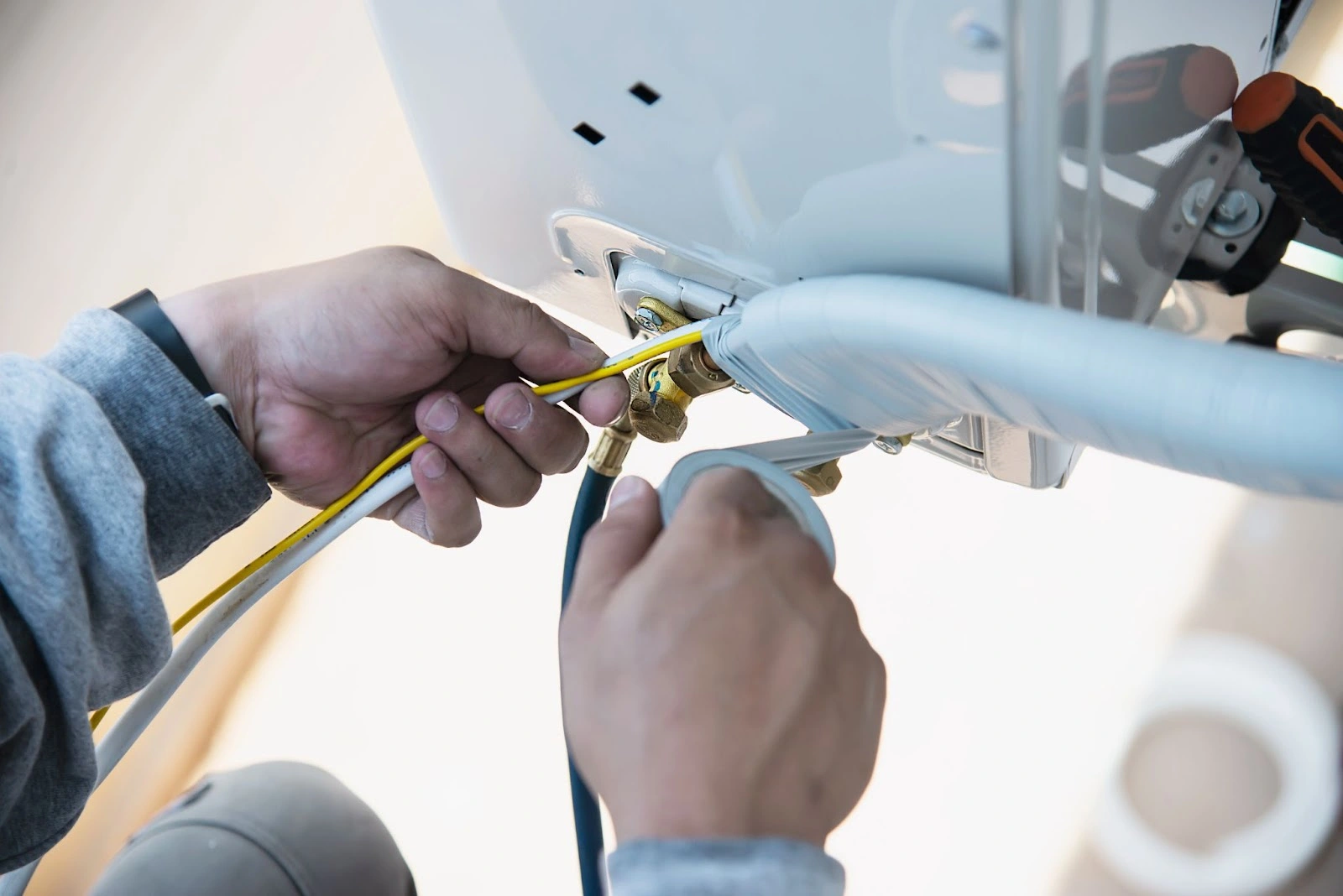 Person installing a white air conditioning unit on a ceiling, securing wires with tape.