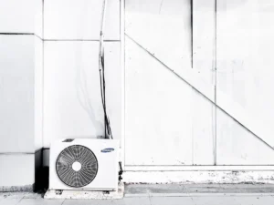 Outdoor AC compressor unit against a white wall, showcasing potential issues such as ice or debris buildup, relevant for diagnosing HVAC problems and repair guidance.