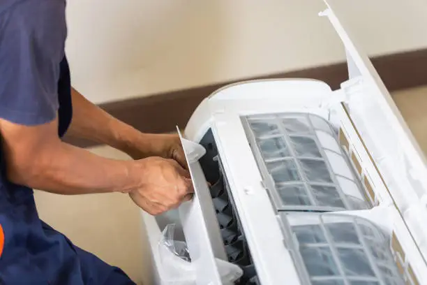 Technician repairing or cleaning the interior components of a wall-mounted air conditioning unit, focusing on the filters and vents.