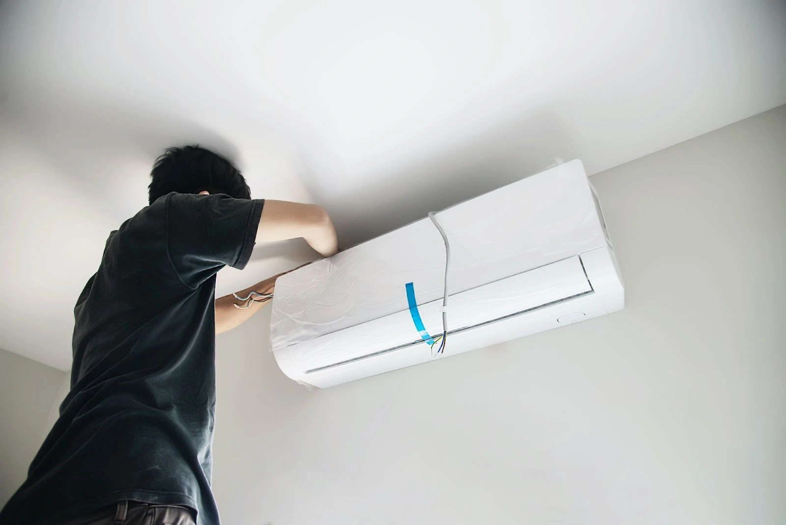 Person installing a white air conditioning unit on a ceiling, securing wires with tape.