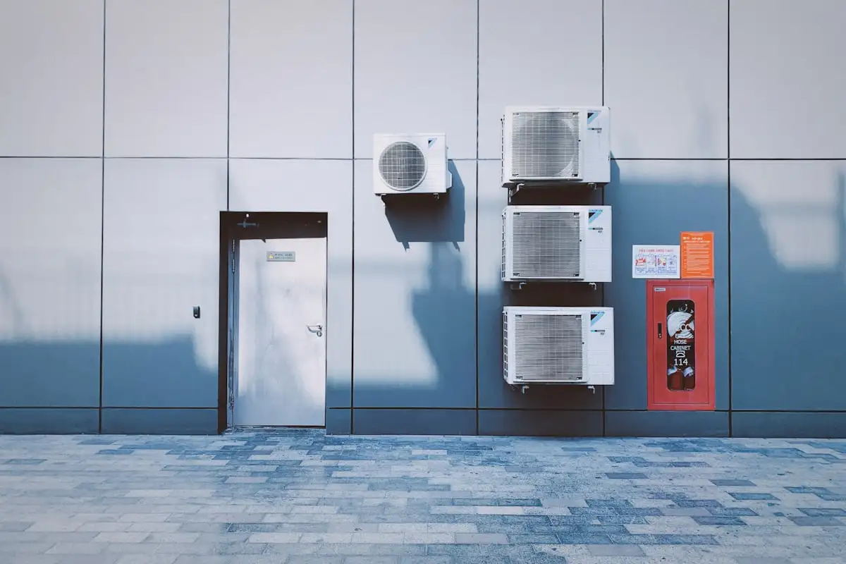 Building wall with multiple air conditioning units and a door, next to a red fire hose cabinet.