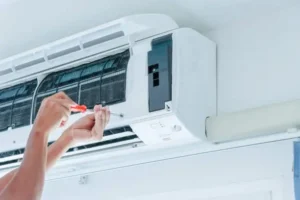 Technician using a screwdriver to service an air conditioning unit, illustrating common maintenance tasks to address AC cooling issues.