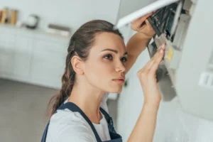 Woman inspecting and adjusting a thermostat, representing troubleshooting for air conditioning issues related to warm air output.