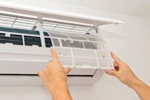 Hands removing a clean air conditioner filter from a wall-mounted unit, emphasizing the importance of filter maintenance for optimal cooling performance.