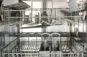 Interior view of an empty dishwasher showing upper and lower racks with metal tines and worn vinyl coating.